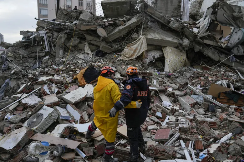 A photo of rescue workers on the rubble of a fallen building looking for survivors. 