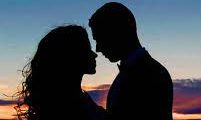 A couples silhouette as they stand enjoy their time together during a sunset