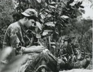 Robert "Bob" Williams fighting in Vietnam War, hiding behind bush, working on a drawing.