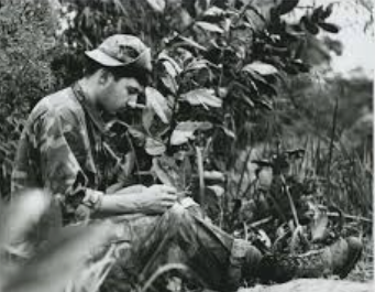 Robert "Bob" Williams fighting in Vietnam War, hiding behind bush, working on a drawing.